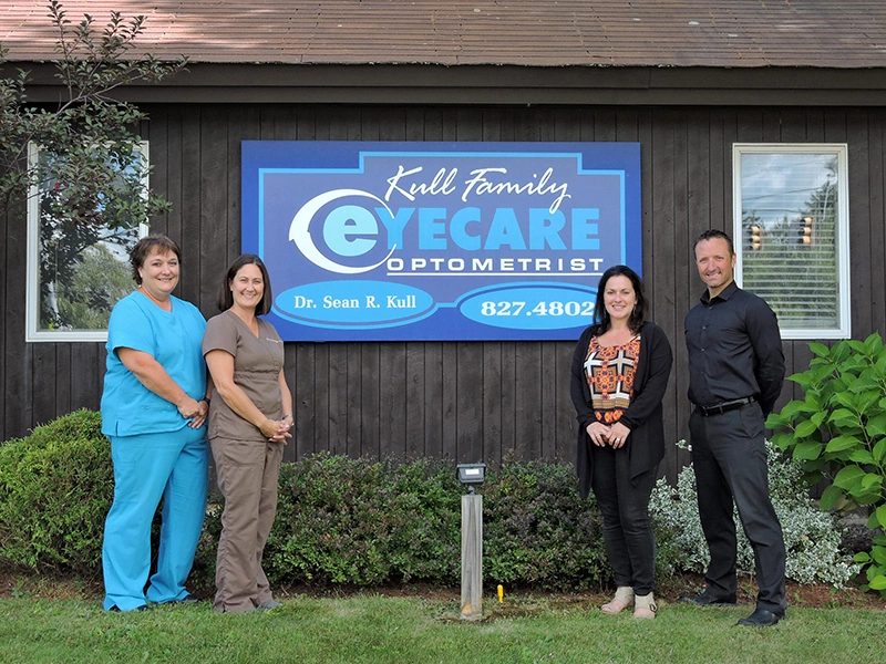 photo of employees at kull family eyecare optometrist standing outside their building in front of a large sign with the name of the business on it