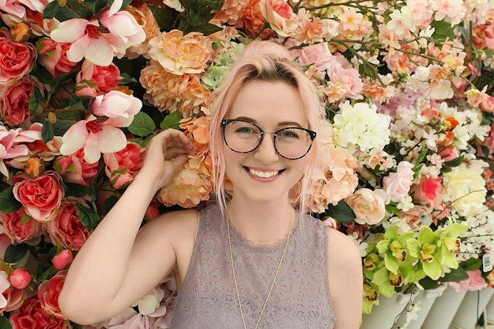 photo of a woman wearing glasses standing in front of a display of flowers