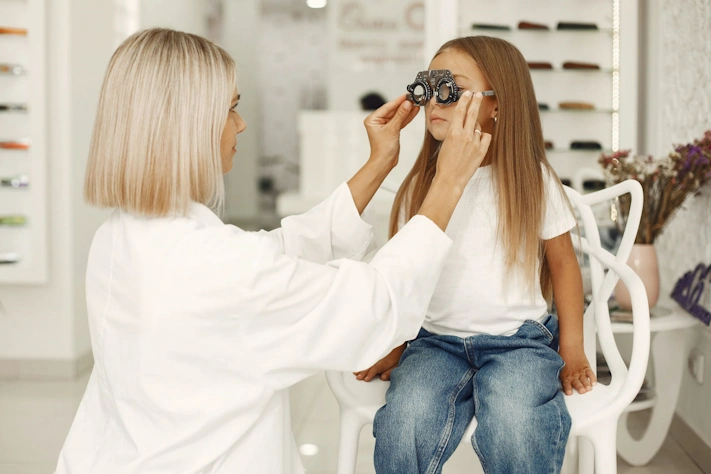 photo of a female optometrist placing optometry tool glasses on face of small girl