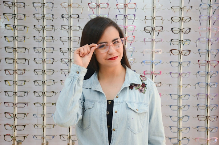 photo of woman wearing glasses in front of a display covered in glasses with different frames